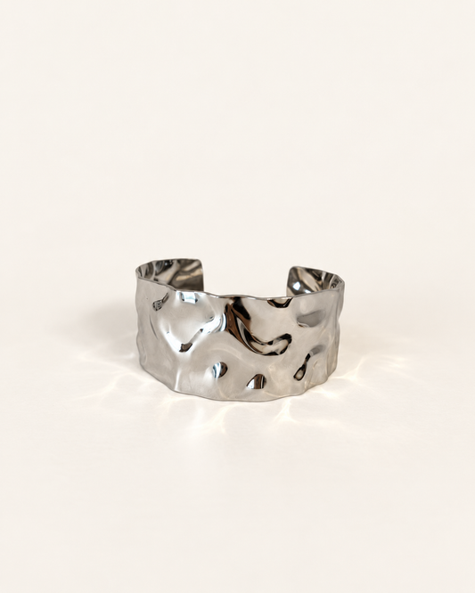A hammered silver cuff bracelet with an organic, textured surface, photographed on a clean off-white background.