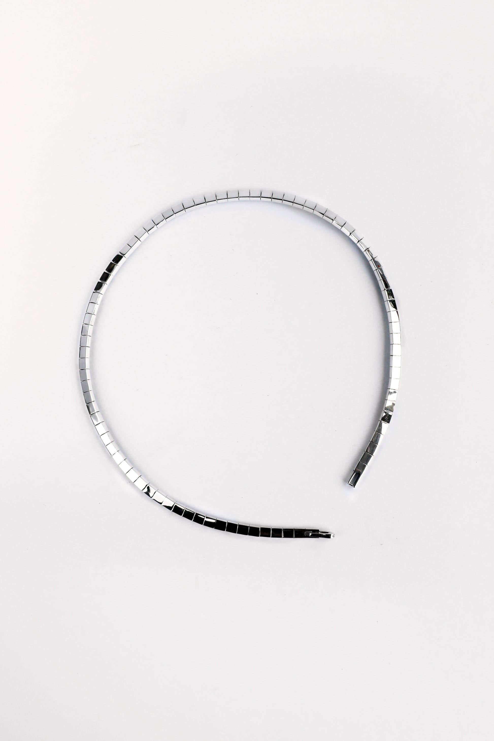 Flatlay of fluid sterling silver segmented necklace in circular shape on white background