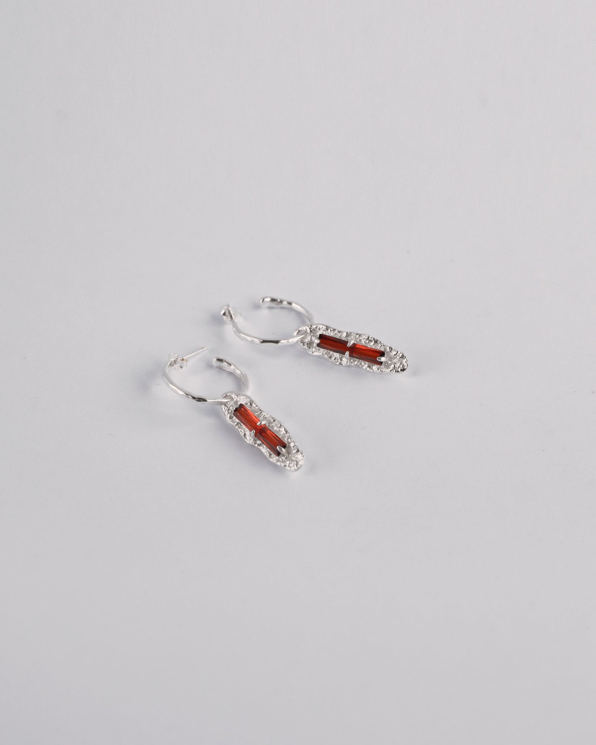 Angled view of red cubic zirconia earrings in sterling silver setting