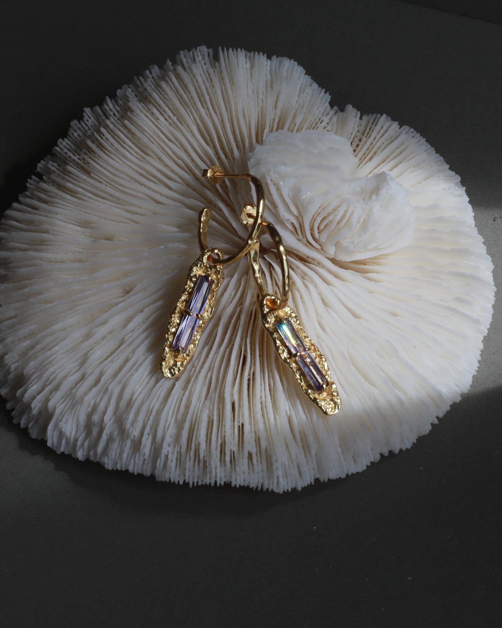 Twilight Gleam gold and purple zircon earrings styled on coral texture for jewelry photography