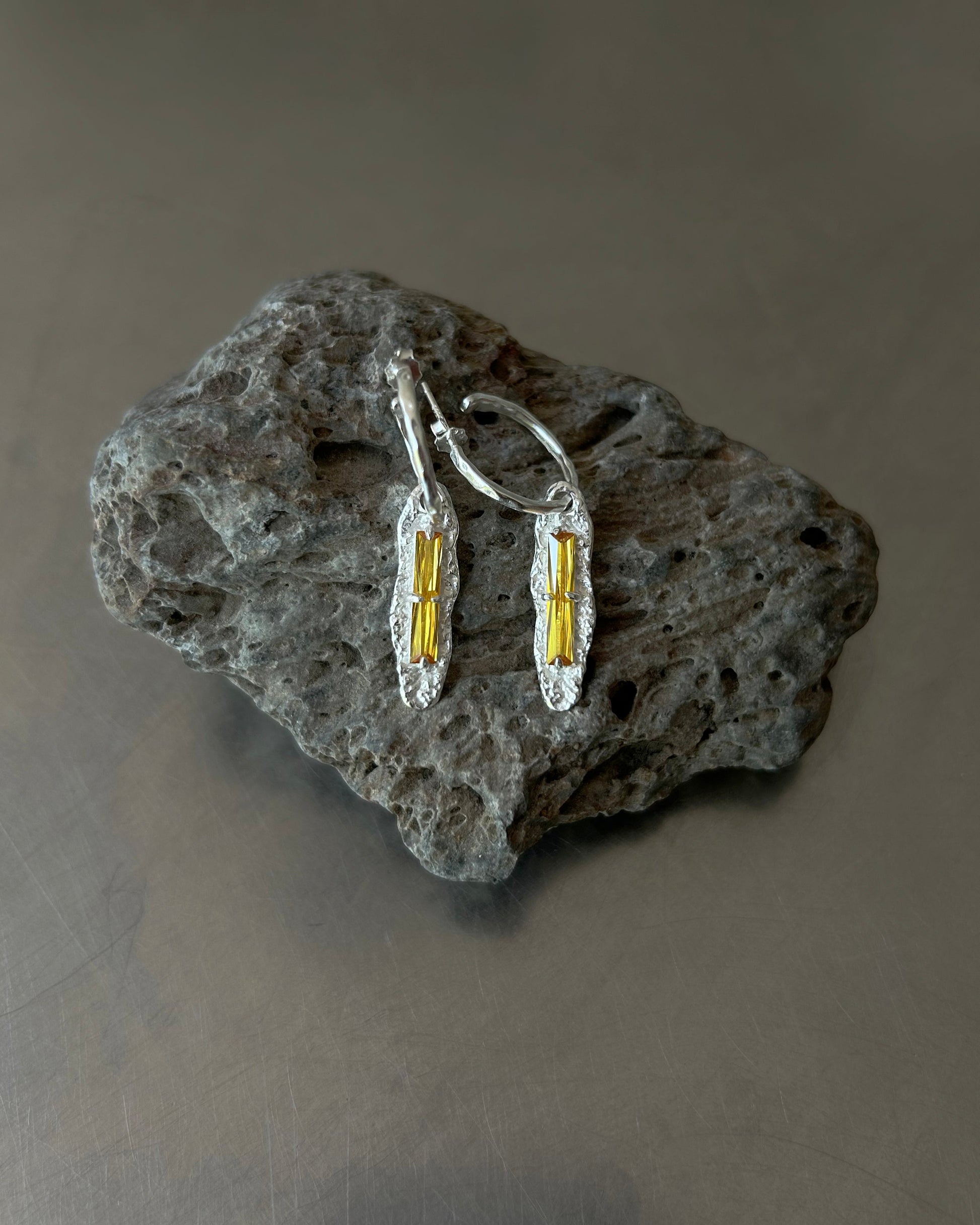 Yellow zircon drop earrings displayed on textured volcanic stone

